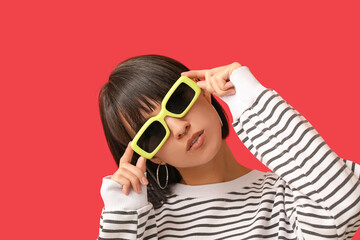 Stylish young woman in sunglasses with nose piercing on red background