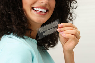 Young woman holding teeth whitening strips on light background, closeup