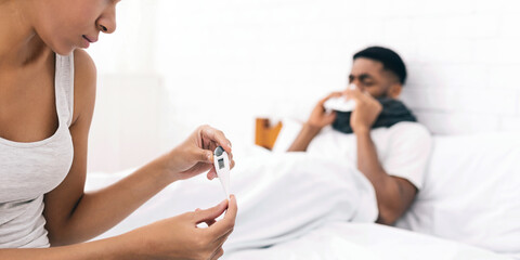 Woman taking care of sick man with fever lying in bed