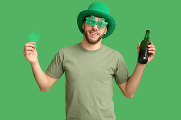 Young man in leprechaun hat with bottle of beer and clover on green background. St. Patrick's Day...
