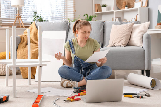 Beautiful young stressed woman with manual and laptop assembling furniture at home