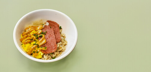 Breakfast bowl with carmalized fired spam, topped with spice dijon mustard, rice and egg, copy space, green background