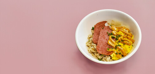 Filipino breakfast bowl with carmalized fired spam, topped with spice dijon mustard, rice and egg, copy space, pink background