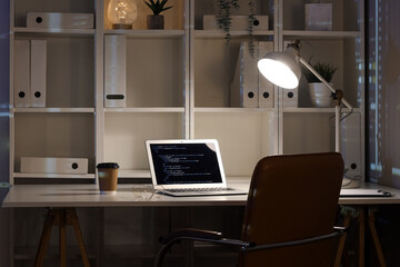 Laptop with programming code on table in dark office