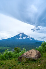 A viewpoint with a large stone and a view of the sacred volcano Agung covered with clouds on a rainy day on the island of Bali. View of the mountain.