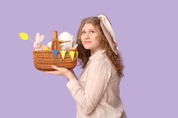 Beautiful young thoughtful woman in bunny ears with Easter basket on purple background