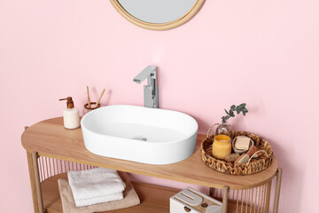 Modern sink with bath supplies on shelving unit near pink wall in bathroom