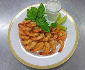 shrimp with sauce and lime wedges on a round white plate, garnished with sprigs of fresh basil. delicious food or snack for beer. healthy, protein-rich seafood