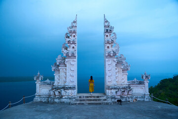 A woman in a yellow dress stands at a famous Balinese traditional gate on the island of Nusa Penida.