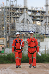 Two skilled engineers confidently stride through the oil and gas refinery, clutching crucial blueprints, embodying industry expertise and determination.