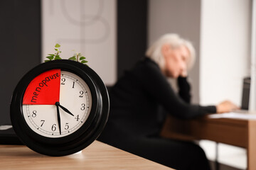 Clock with word MENOPAUSE on table in office, closeup