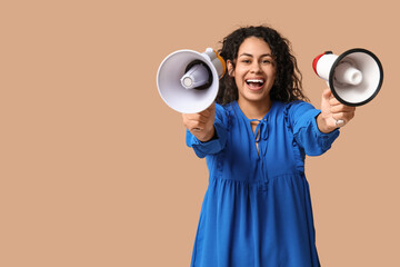 Young African-American woman with megaphones on beige background