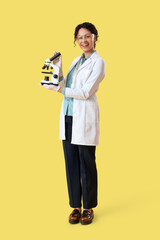 Female African-American chemist with microscope on yellow background