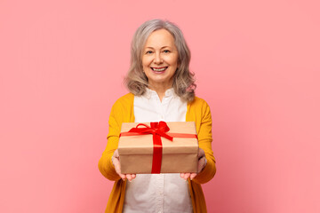 Elegant retired mature lady poses giving wrapped present box, studio