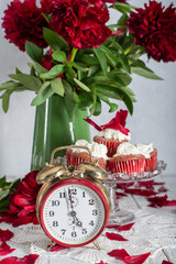 still life in English style with scarlet peonies and red velvet cupcakes with on a platter,tea time on red antique clock