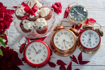 collection of vintage watches on the table, red velvet cupcake on a platter, scarlet foam petals on a white tablecloth