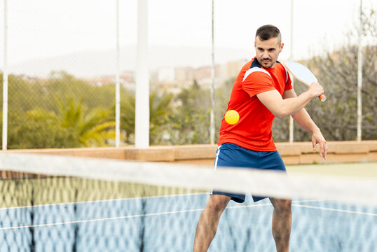 An adult man in sportswear is playing a game of pickleball on an outdoor court.The man is making a backhand with the racket to hit the ball.Pickle ball concept. Men Playing Pickleball