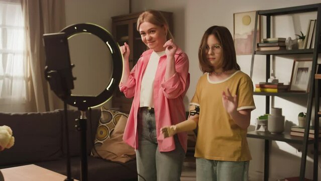Full medium footage of modern Caucasian mom and daughter with artificial arm recording trendy dance challenge on cell phone using circular lamp at home