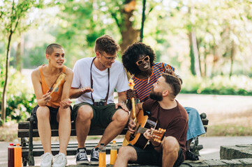 Interracial friends sitting in a park and listening guitar player.