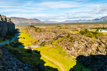 An expansive view of the geological rift at Thingvellir National Park in Iceland, showcasing the distinct landscape marked by rugged terrain and lush greenery under a clear blue sky. Iceland