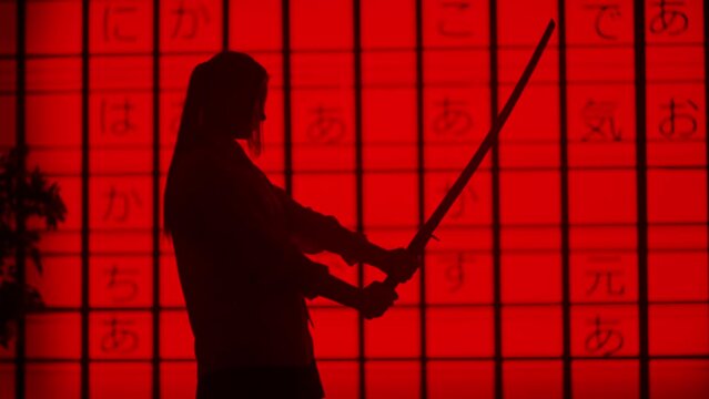 Person against big digital wall in studio. Silhouettes of woman acting with japanese sword katana in front of digital screen red asian graphic background.