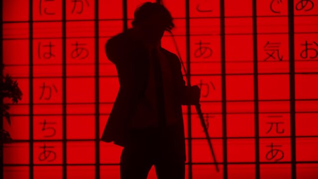 Person against big digital wall in studio. Silhouettes of man acting with japanese sword katana in front of digital screen red asian graphic background.