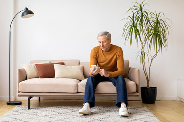 Senior man sitting on couch using smartphone