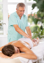 Obraz na płótnie Canvas Elderly male masseur doing anti-cellulite massage to female patient lying at massage table