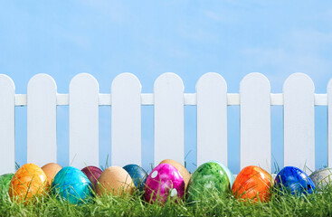 Spring grass and wooden fence with easter eggs on cloudy sky - 769156324
