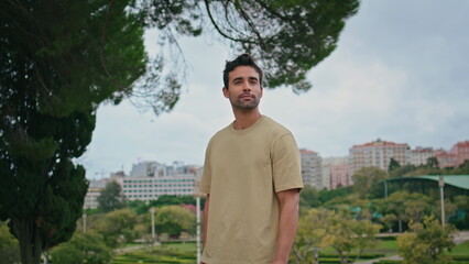 Latin guy posing green park in front cityscape close up. Man looking camera 