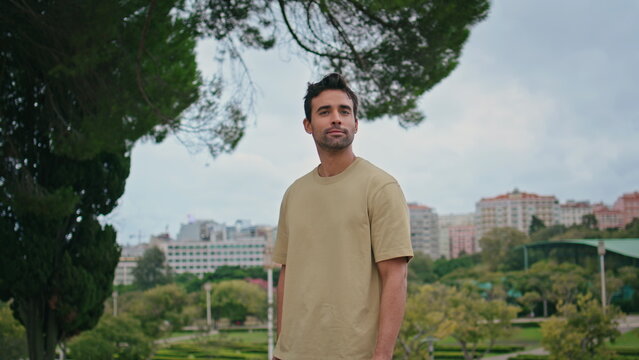 Fototapeta Latin guy posing green park in front cityscape close up. Man looking camera 