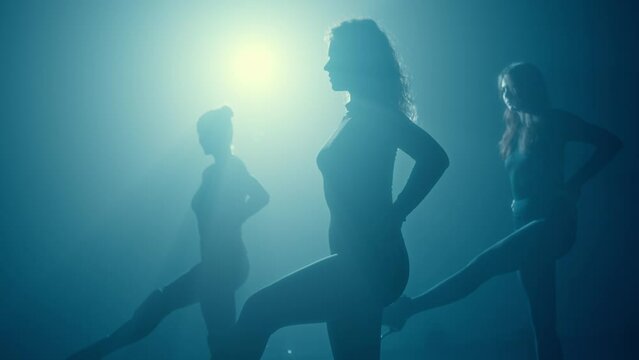 Three young women in silhouette, captured sensually dancing against a vibrant blue backlight.