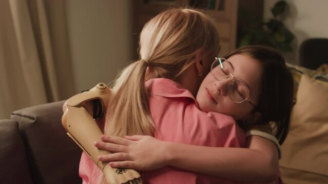 Back slowmo of little girl in glasses and with bionic plastic arm hugging her mother while spending time together at home