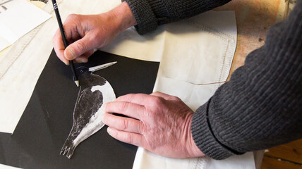 A tailor uses his hand and a pencil to trace a stencil of a bird motif on a black canvas
