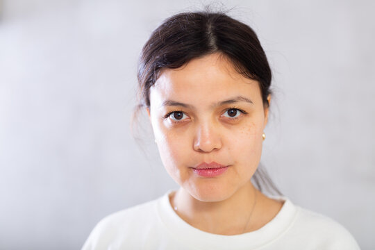 Closeup portrait of focused serious young brunette with hair tied back in bun, looking at camera confidently. Studio photoshoot on gray background