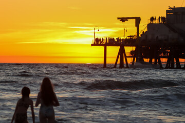 Dozens of Distant People, Plus Two Girls in Foreground,  Watching Bright Yellow and Orange Sunset,...