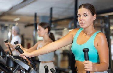 Young woman in sportswear training on elliptical machine in gym