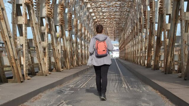 Walking woman on rusty bridge. A view of walking female with backpack on railway bridge.