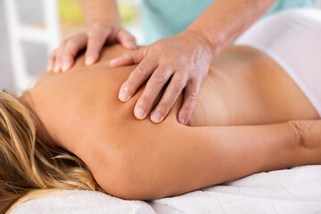 Hands of mature masseuse doing back massage procedure for woman patient in therapy cabinet