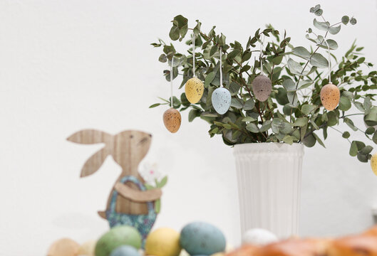 Wooden easter bunny and colorful eggs on a eucalyptus plant in a vase, on table at home