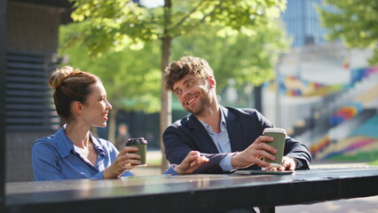 Cheerful employees enjoying coffee break on city street. Happy couple laughing