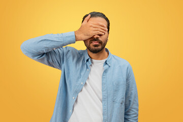 Man covering face with hand on yellow background