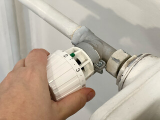 Close up of a hand turning the thermostat radiator at the middle position. Heating of houses in the cold season