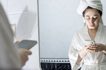 Portrait of a young latina woman chatting on her cell phone in front of the mirror at home before having a beauty treatment.