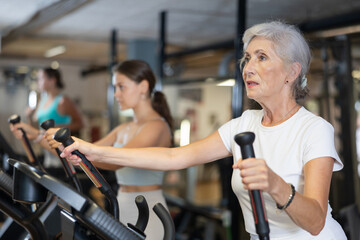 Active athlete senior woman engaged in intensive high interval training on ellipsoid simulator. Training of respiratory and cardiovascular system, increasing endurance in crossfit gym