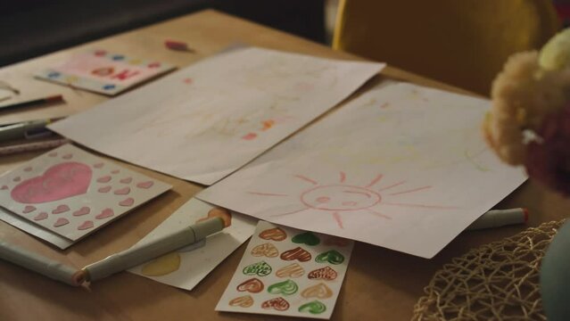 No people footage of childrens multiple drawings of sun and hearts on table with color markers and flowers in vase at home
