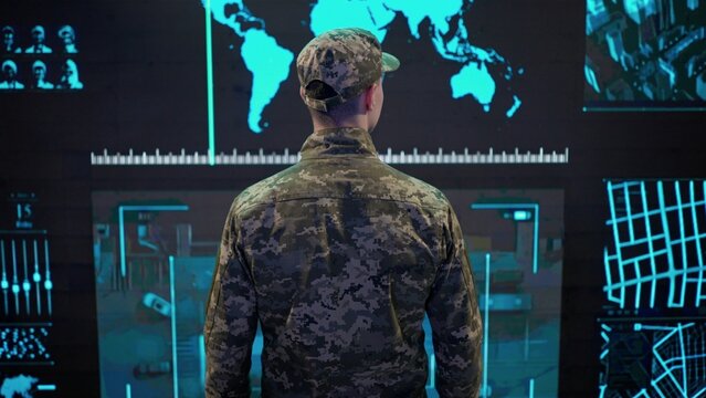 Control center. Military headquarters surveillance officers cyber police working in office, young soldier looks at information on a large digital screen. Rear view.