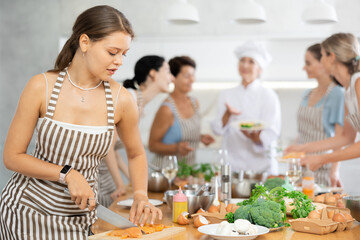 Young woman in apron learns to cook chicken dish at cooking master class