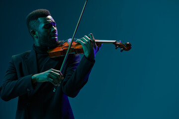 Elegant African American man in suit playing violin against blue background, classical music performance concept