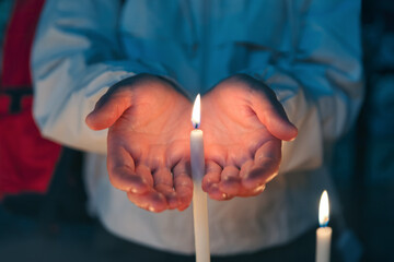 Woman hands holding burning candle in church at night